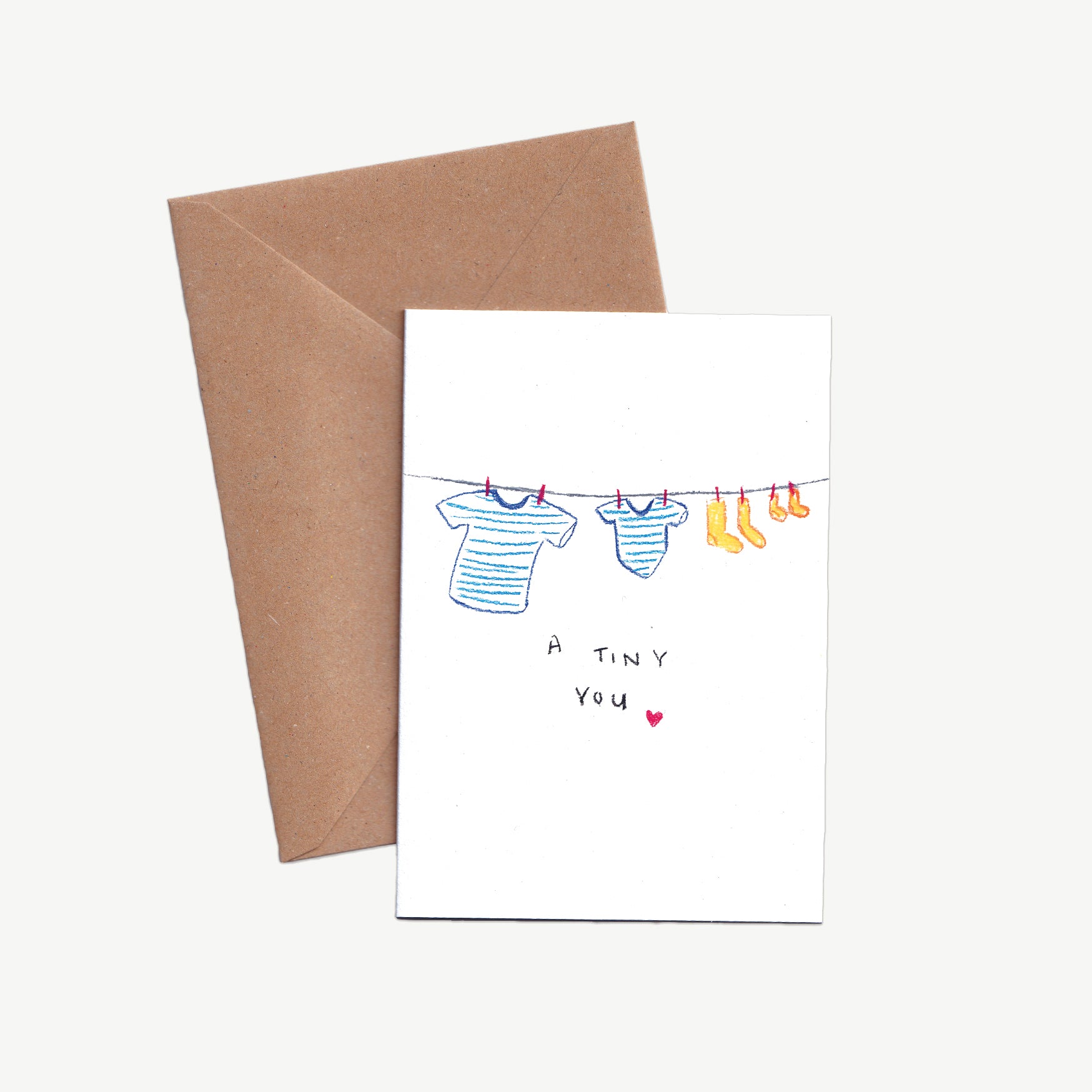 A Greetings Card with a washing line, little and large blue striped t-shirts and little and large yellow socks with the words 'a tiny you' and a heart, drawn in pastel pencil, with a kraft brown envelope 