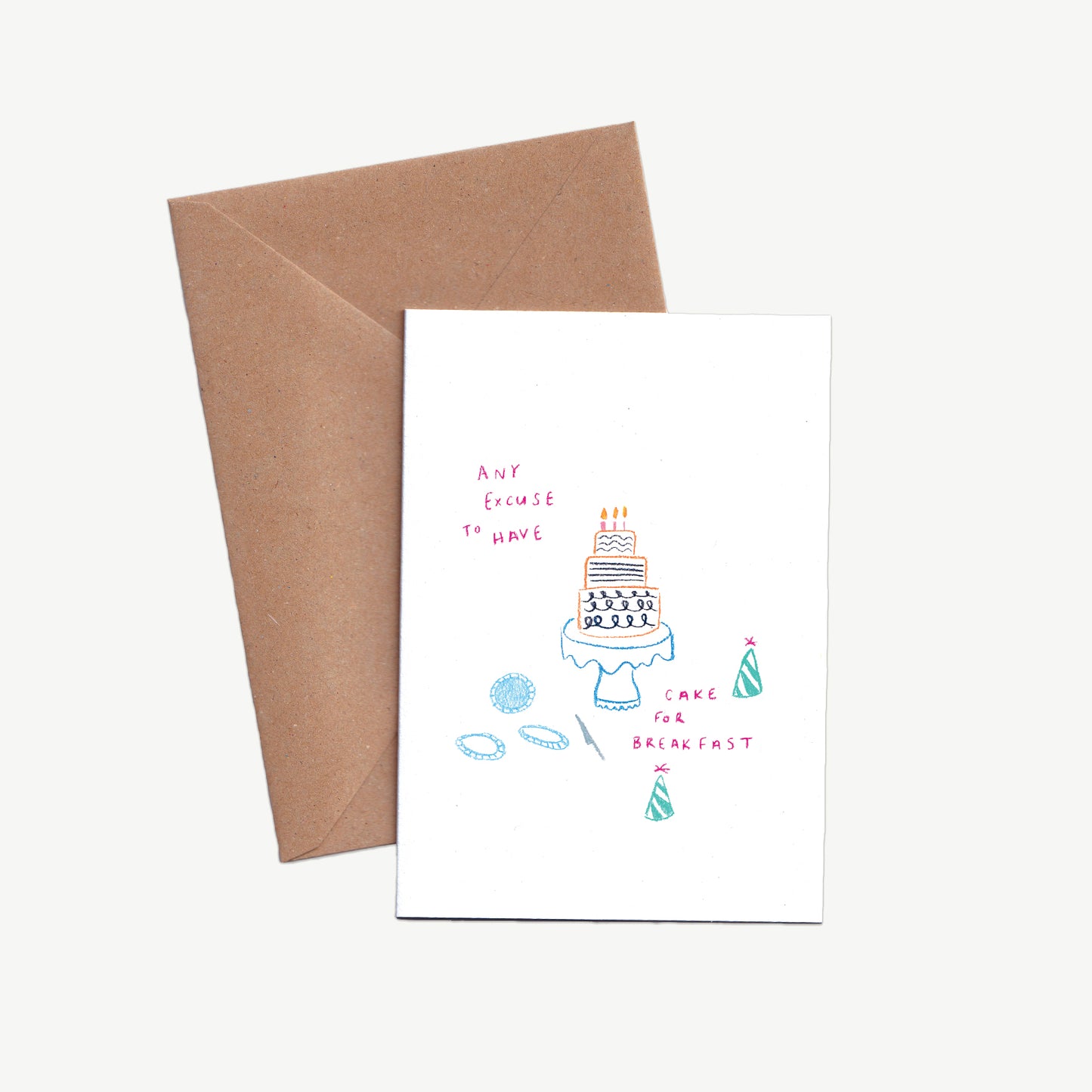 A Greetings card with a birthday cake on a cake stand, with party hats and plates, the words 'any excuse to have cake for breakfast' written in pink pencil, displayed with a kraft brown envelope